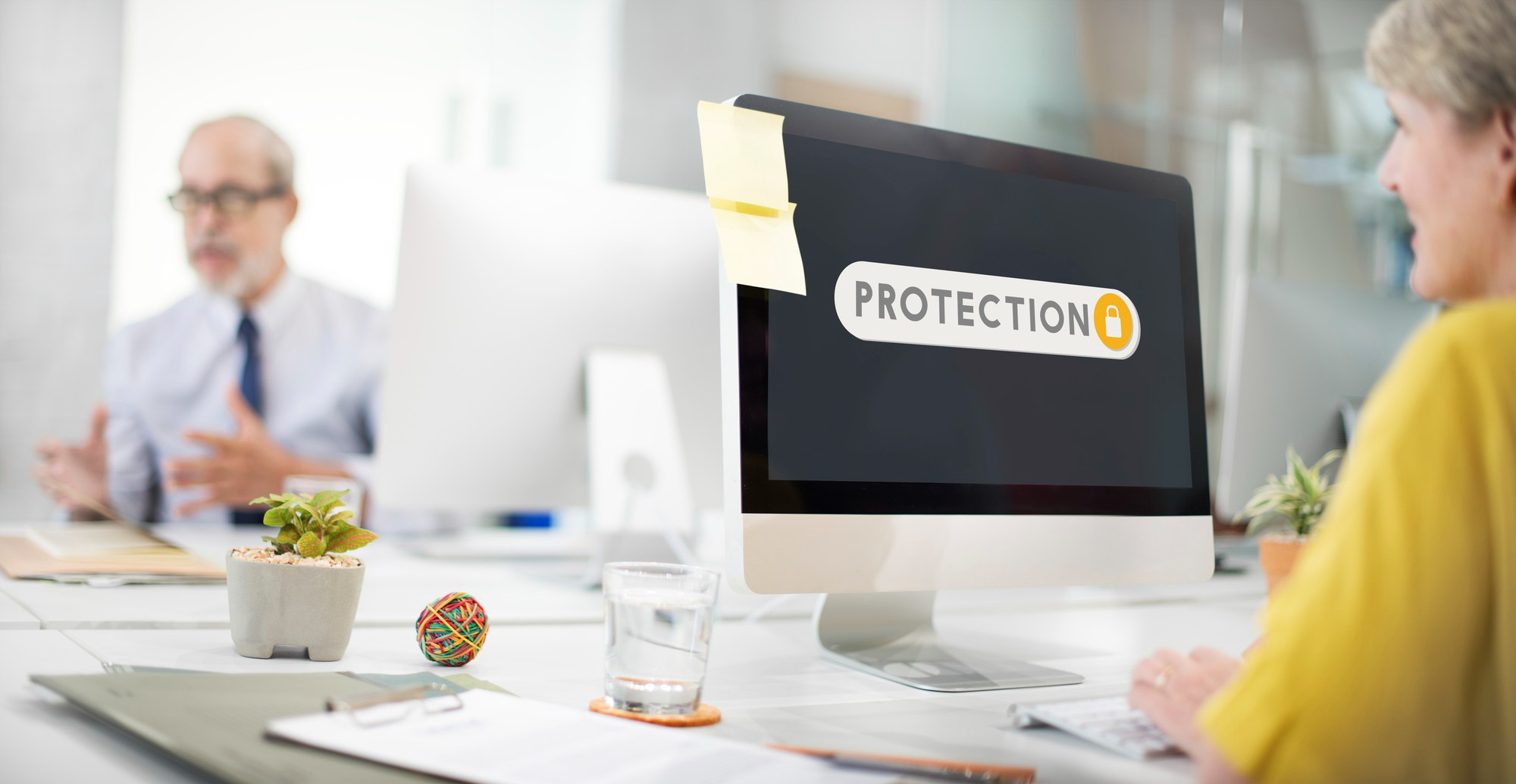 due persone in azienda un po' sfocate e a fuoco si vede un monitor con la scritta "protection"