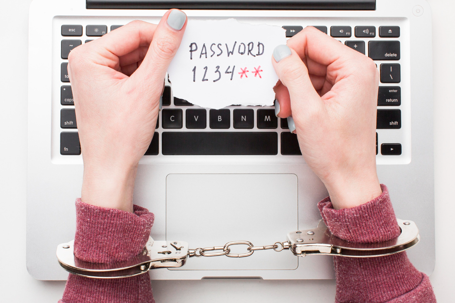 delle mani ammanettate che tengono tra le mani un foglietto con una password